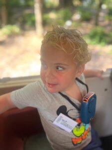 Little boy named Cooper wearing a Mickey Mouse shirt, smiling while looking out of a Disney park tram window.