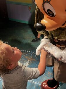 Young boy named Cooper looks up in awe while holding hands with Mickey signing his autograph book at Walt Disney World.