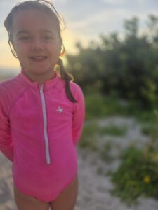 Young girl smiling in a pink swimsuit at sunset on the beach during her dream trip to Florida