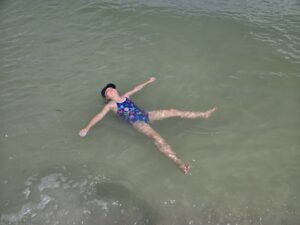 Girl floating peacefully on her back in the ocean wearing a colorful swimsuit and dark cap