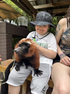 Nathan smiling while gently holding a red ruffed lemur on his lap at Myrtle Beach Safari.