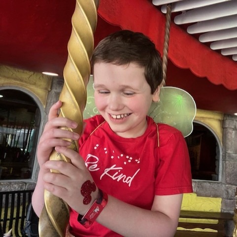 Mylo smiling while riding the carousel at Give Kids the World Village, wearing fairy wings and showing his Mickey tattoo during his dream trip.