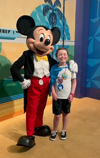 Mylo grinning while standing beside Mickey Mouse at Disney World, celebrating his dream vacation with Toby’s Dream Foundation.